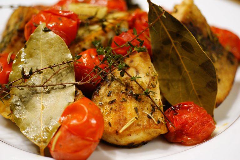 Involtini di pesce spada con foglie di alloro e pomodorini in un piatto bianco